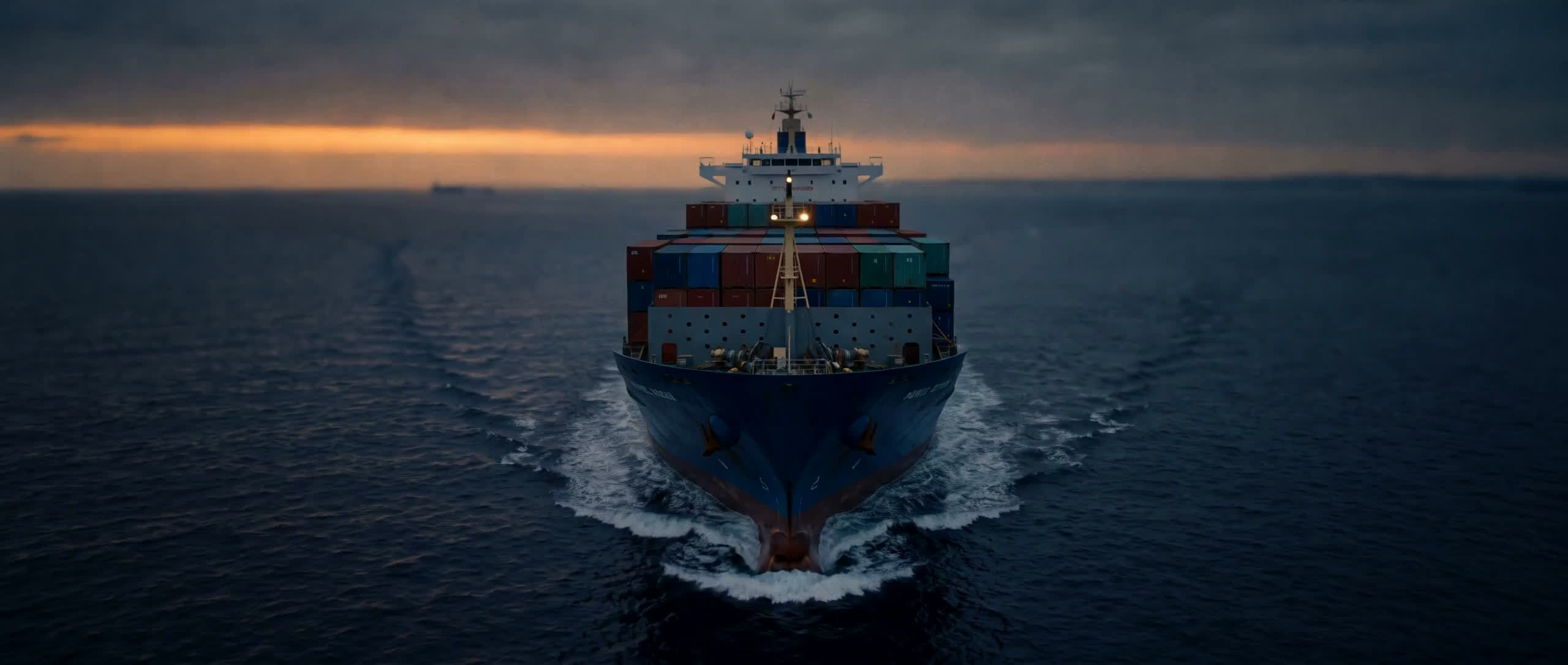 Aerial view of a cargo ship under way, leaving a long wake across open water.