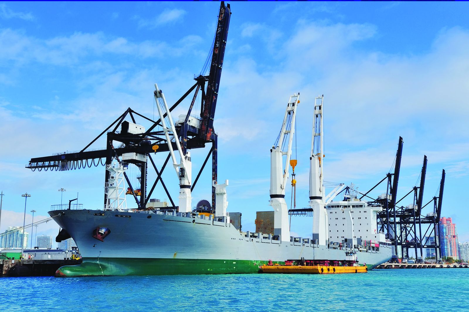 A heavy-lift vessel alongside, working under shore cranes.